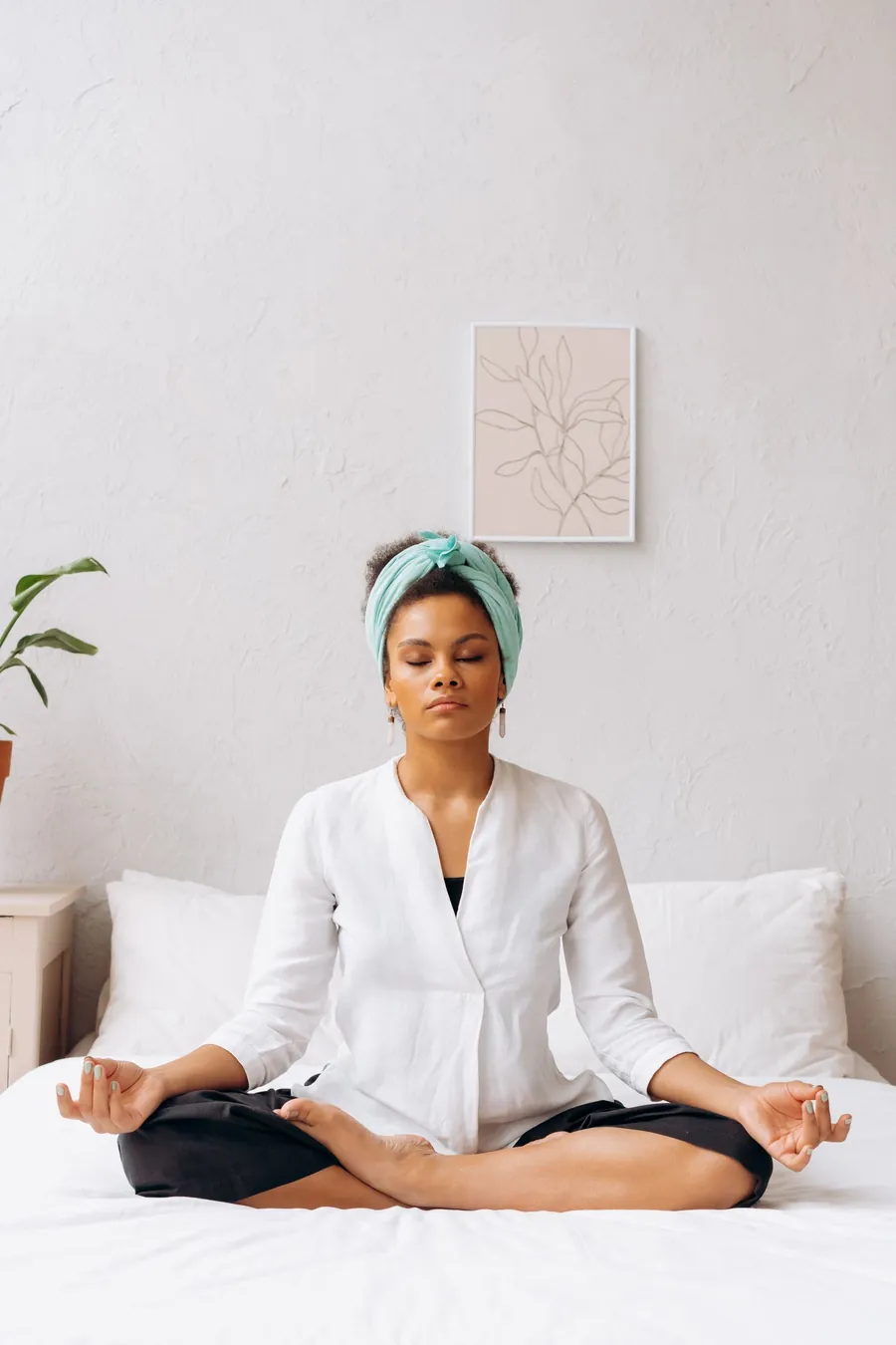 Breathing exercise to fall asleep fast: woman sitting cross-legged on her bed, eyes closed